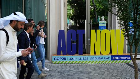 A group walks near a sign that reads "act now" at the COP28.