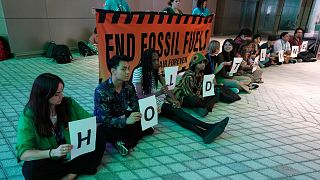 Demonstrators hold signs that reads "hold the line" and "end fossil fuels" during COP28. 