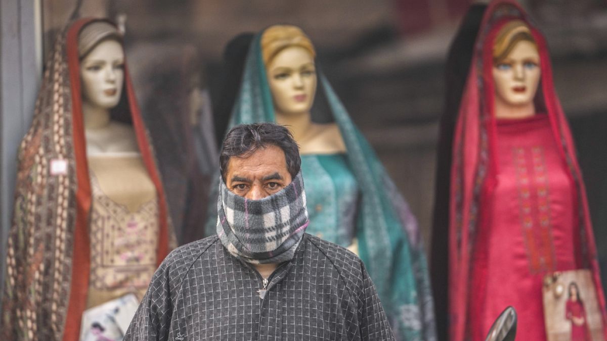 Un uomo ha il volto coperto da un panno di lana mentre attende l'autobus davanti a un negozio di abbigliamento in una giornata fredda a Srinagar