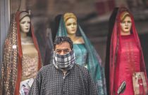 Un uomo ha il volto coperto da un panno di lana mentre attende l'autobus davanti a un negozio di abbigliamento in una giornata fredda a Srinagar