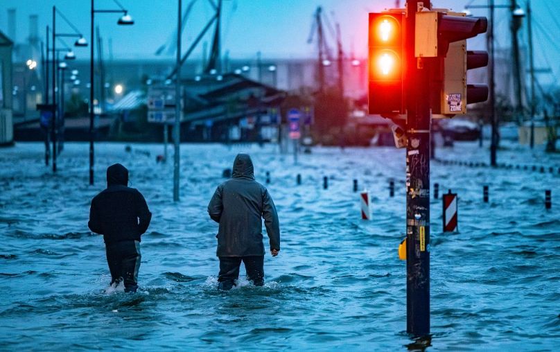 People make their way across a flooded street in Flensburg, Germany in October as Storm Babet causes havoc.