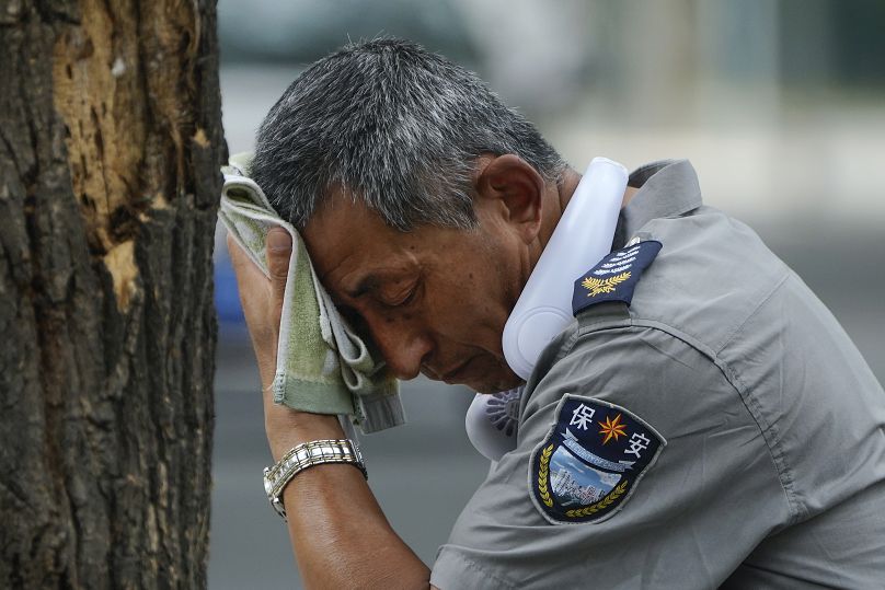 A security guard wearing an electric fan on his neck wipes his sweat on a hot day in Beijing, Monday, July 3, 2023.