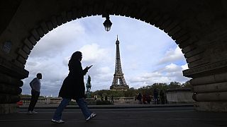 A woman checks her phone as she walks on a bridge, Thursday, Nov. 2, 2023 in Paris. (AP Photo/Aurelien Morissard)