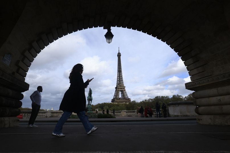 A woman checks her phone as she walks on a bridge in Paris, November 2023