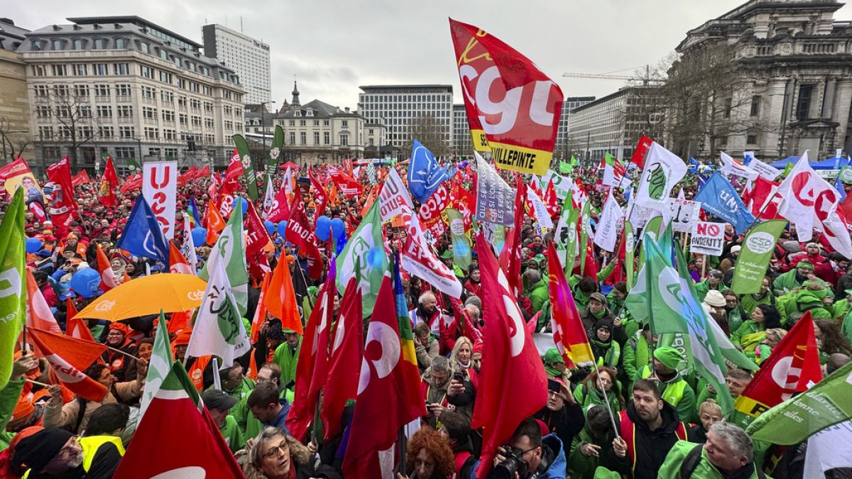 Protestors hold flags and gather during a demonstration against austerity measures in Brussels, Tuesday, Dec. 12, 2023.