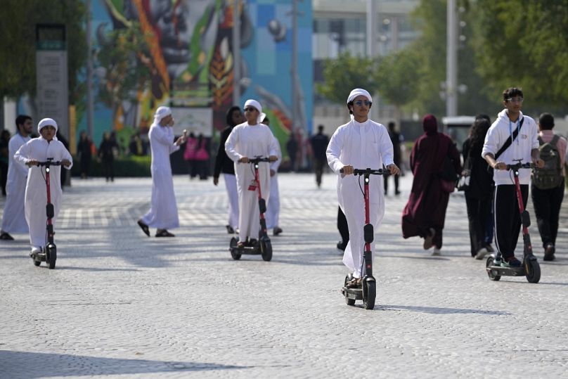 People ride an electric scooter through the COP28 UN Climate Summit in Dubai, December 2023