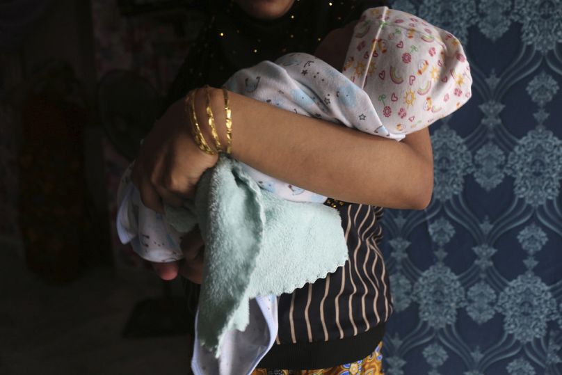 Yaşlı bir adamla 'evlenen' 16 yaşındaki Arakanlı Müslüman kız, kucağında yeni doğan bebeği ile Kuala Lumpur'da bir apartman dairesinin penceresinde dururken