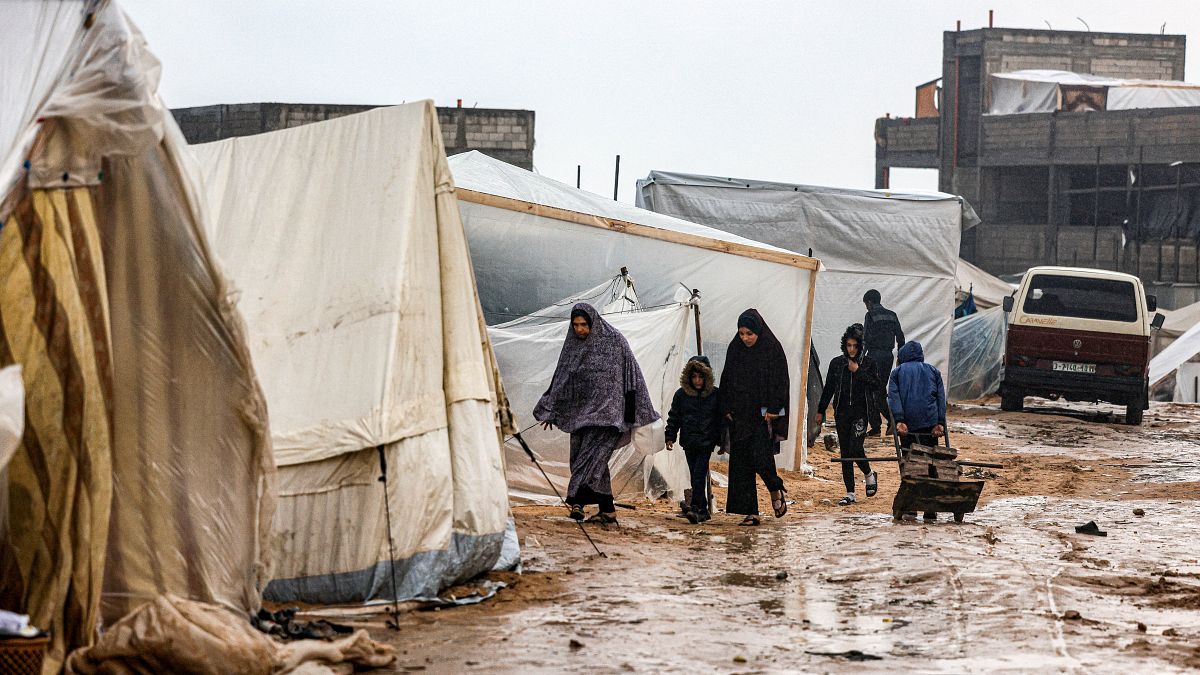فلسطينيون يسيرون تحت المطر في مخيم للنازحين في رفح