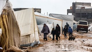 فلسطينيون يسيرون تحت المطر في مخيم للنازحين في رفح