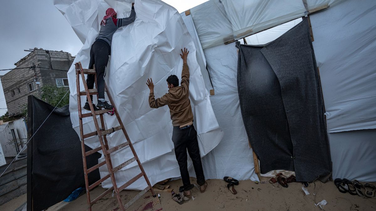 نازحون فلسطينيون يحاولون حماية خيامهم خلال هطول الأمطار في مخيم في رفح