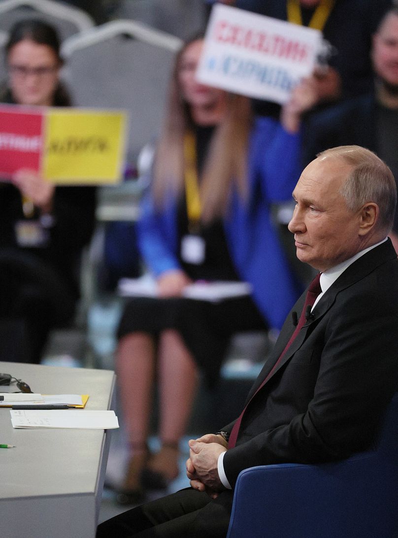 Journalists hold placards to attract the attention of Russian President Vladimir Putin at his year-end press conference