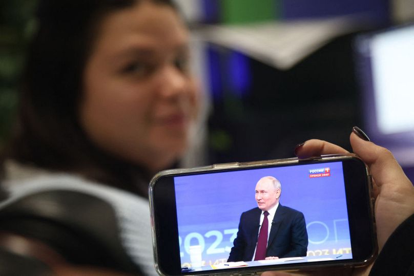 A woman watches a live broadcast of Russian President Vladimir Putin's year-end press conference on a smartphone in an office in Simferopol, Crimea