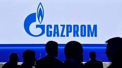 Participants walk in front of a large screen displaying the logo of Russia's energy giant Gazprom during the St. Petersburg International Gas Forum (SPIGF) in Saint Petersburg