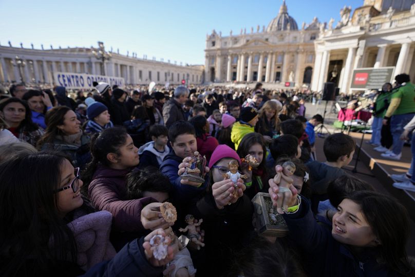 Children hold up statues of baby Jesus as they wait for Pope Francis' Angelus noon prayer