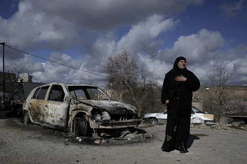 امرأة فلسطينية تقف بجانب سيارة محترقة، في قرية جالود القريبة من مدينة نابلس بالضفة الغربية المحتلة.