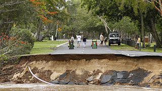Stranded residents stand on a road, a large section of which has washed away, in the suburb of Holloways Beach in Cairns, Australia, Monday, Dec. 18, 2023.