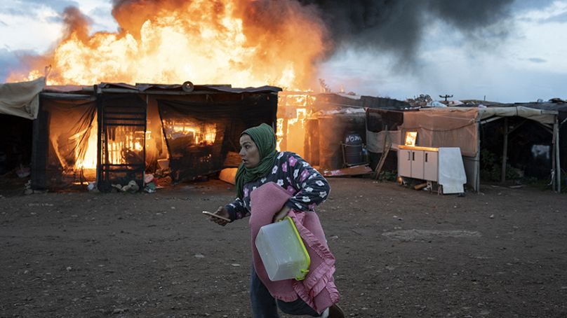 A woman runs past burning shacks during a fire before an eviction by police officers in Almeria, Spain, Monday, Jan. 30, 2023.