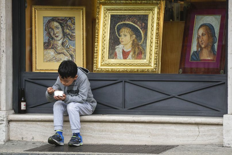 A child enjoys his ice cream sitting by a shop window selling religious items in Rome, January 2023