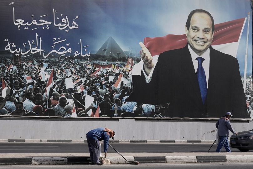 Workers clean the street under a billboard supporting Egyptian President Abdel Fattah el-Sissi for the presidential elections, in Cairo.