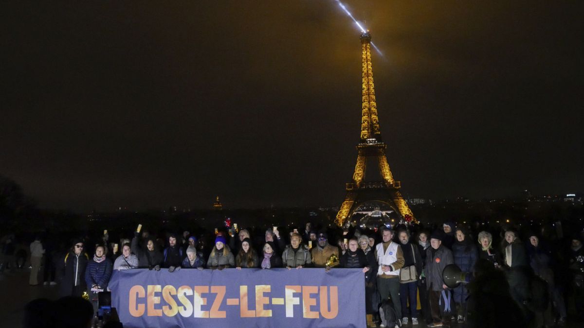 Menschen halten vor dem Eiffelturm ein Plakat mit der Aufschrift "Feuer einstellen", um eine Feuerpause in Gaza zu fordern, Montag, den 18. Dezember 2023, in Paris.