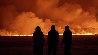 Tres personas observan el cielo iluminado por la erupción de un volcán en Grindavik, en la península islandesa de Reykjanes.