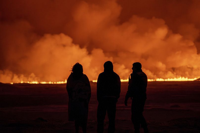 People watch as the night sky is illuminated caused by the eruption of a volcano in Grindavik on Iceland's Reykjanes Peninsula,