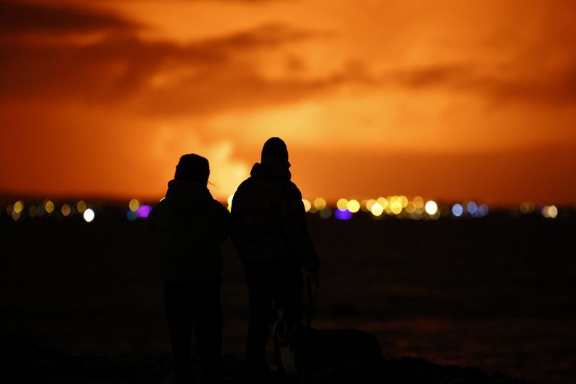 Varias personas observan la iluminación del cielo nocturno provocada por la erupción de un volcán en la península de Reykjanes, en el suroeste de Islandia.