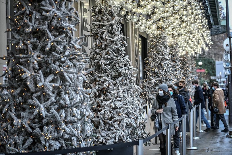 Des personnes masquées devant les vitrines illuminées d'un grand magasin à Paris le 24 décembre 2020, à la veille de Noël, en pleine pandémie de Covid-19.