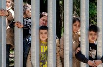 Members of a group of some 30 migrants seeking asylum are seen in Bialowieza, Poland, on Sunday, 28 May 2023 across a wall that Poland has built on its border with Belarus. 