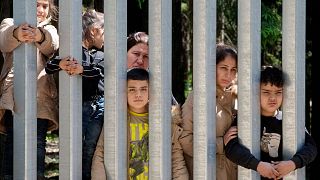 Members of a group of some 30 migrants seeking asylum are seen in Bialowieza, Poland, on Sunday, 28 May 2023 across a wall that Poland has built on its border with Belarus. 