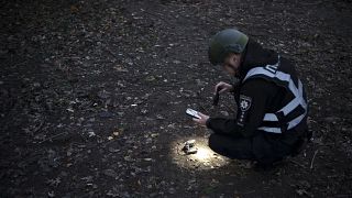 ضابط شرطة أوكراني يستخدم مصباحًا يدويًا للبحث عن حطام طائرة بدون طيار بالقرب من موقع انفجار عقب هجوم روسي بطائرة بدون طيار