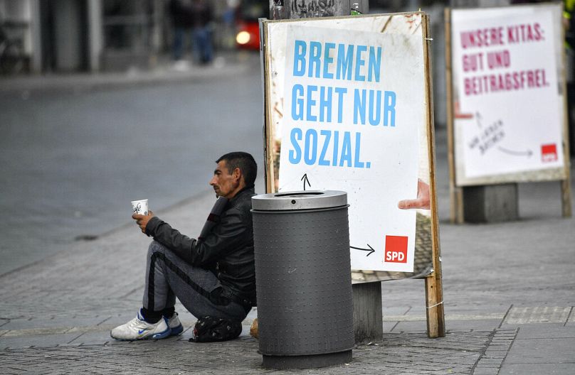 A man begs in front of an SPD poster reading 'Bremen works only social' for the regional elections in the center of Bremen, Germany, Tuesday, May 14, 2019.