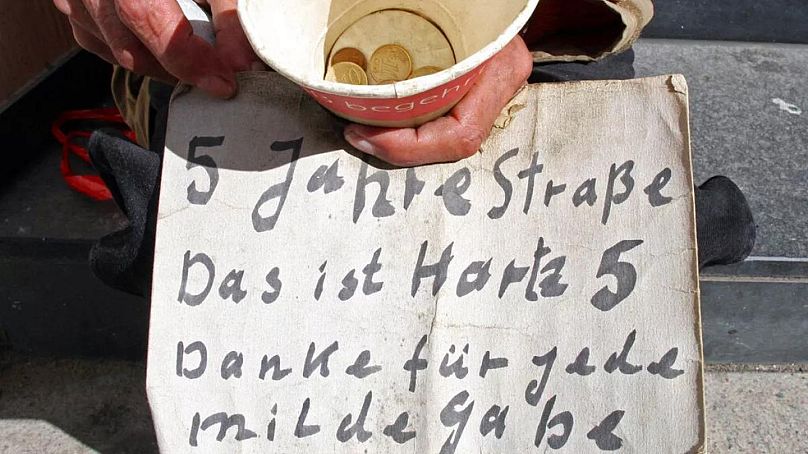 یک فرد بی‌خانمان در آلمان که روی مقوایی نوشته: ۵ سال در خیابان