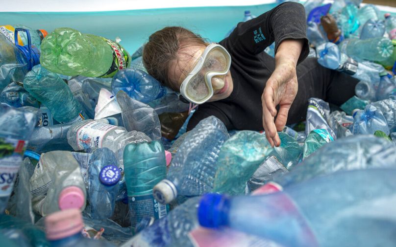 An activist mimics swiming in an inflatable pool filled with PET plastic bottles during a protest outside the environment ministry in Bucharest, June 2021
