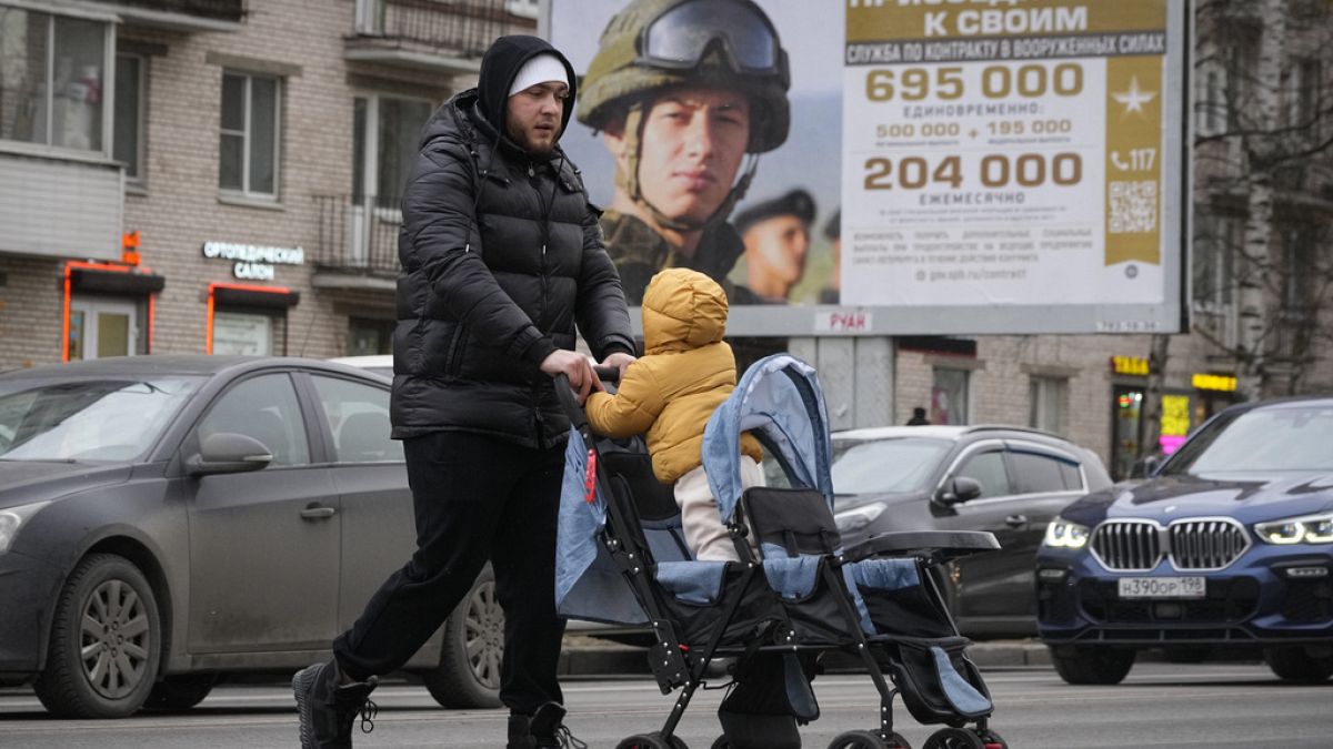 Un hombre y su hijo pasan junto a un cartel de reclutamiento del ejército en Moscú 