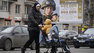 Un hombre y su hijo pasan junto a un cartel de reclutamiento del ejército en Moscú 
