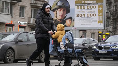 A man and his child pass an army recruitment poster in Moscow 