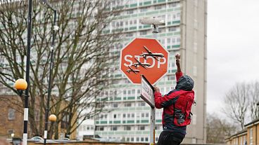 A person removes a piece of art work by Banksy, which shows what looks like three drones on a traffic stop sign
