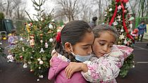 Due bambine si abbracciano davanti a un albero di Natale a Bucarest, in Romania