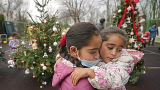 Due bambine si abbracciano davanti a un albero di Natale a Bucarest, in Romania