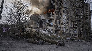 Un policía ucraniano se pone a cubierto frente a un edificio en llamas alcanzado por un ataque aéreo ruso en Avdivka, Ucrania.