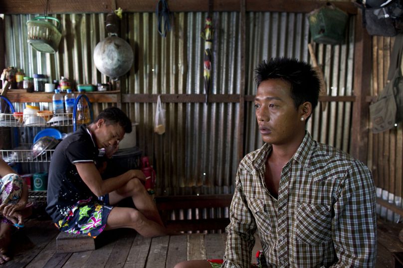 El ex pescador esclavo birmano Lin Lin, a la derecha, habla de sus amigos desaparecidos en el mar mientras Kaung Htet Wai, a la izquierda, fuma un cigarrillo en una choza en las afueras de Yangon, julio de 2015.