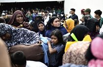 نساء وأطفال من أقلية الروهينغا يحملون ممتلكاتهم في أثناء نقلهم من مأواهم المؤقت في قاعة تابعة للبلدية بعد احتجاج عدد من الطلاب الإندونيسيين ضدهم في باندا آتشيه