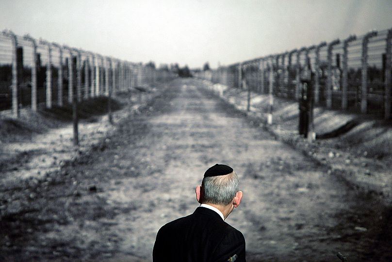 خاخام اسرائیل سینگر، رئیس کنگره جهانی یهودیان به عکسی از اردوگاه کار اجباری آشویتس نگاه می‌کند (آرشیوی)