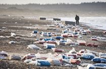 A person walks past stranded containers in the area between Tranum and Slette beach, in Denmark, Saturday, Dec. 23, 2023