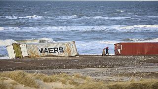 La gente pasa junto a contenedores varados en la playa de Slette, en Dinamarca, el sábado 23 de diciembre de 2023.