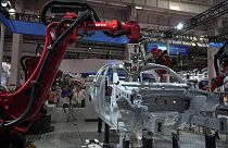 FILE - Visitors look at the robotic arms assembly a vehicle frame during the annual World Robot Conference at the Etrong International Exhibition and Convention Center in the 