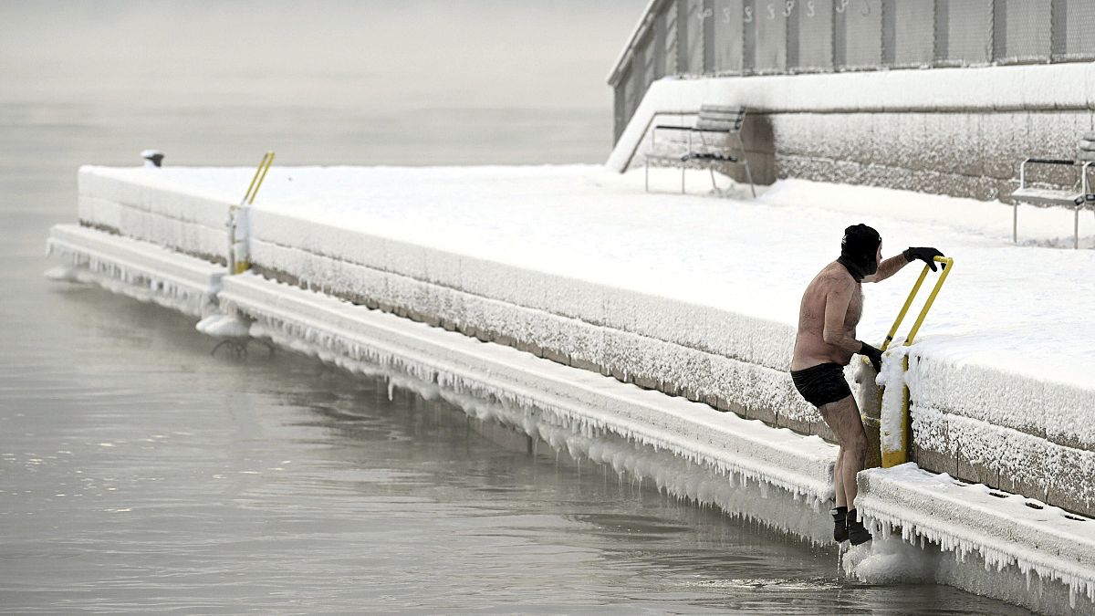 رجل يتسلق من البحر الجليدي إلى الرصيف، في جنوب هلسنكي فنلندا