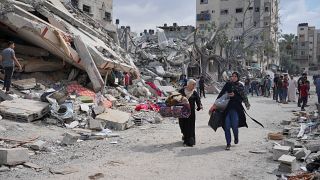 نساء فلسطينيات يسيرن بالقرب من المباني التي دمرتها الغارات الجوية الإسرائيلية في مخيم النصيرات