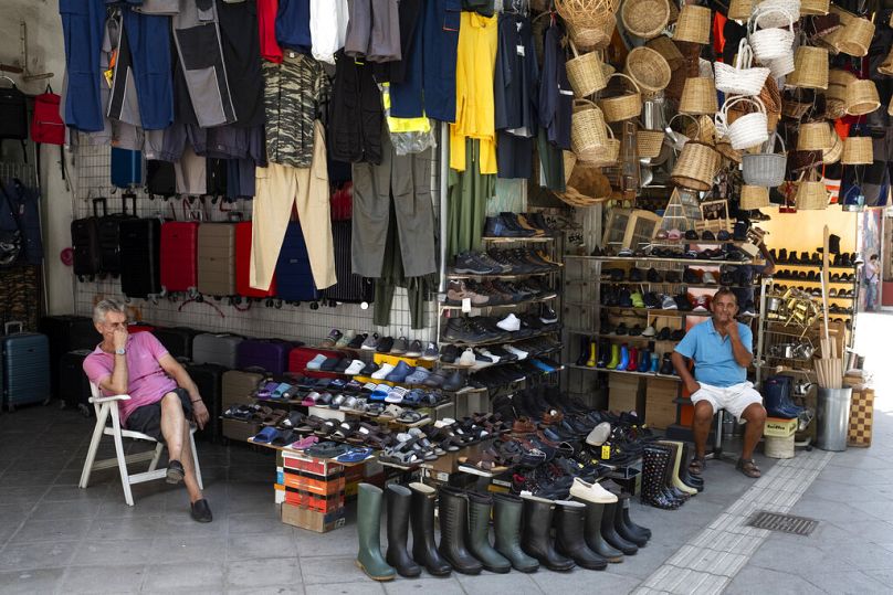 Two vendors sit outside shops at a market street, in Athens